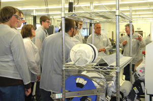 Lenze employee shows area students a surface mount technology board from the production line.