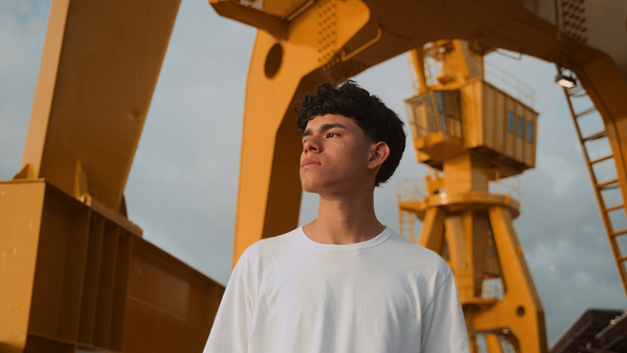 A teen in front of outdoor industrial equipment.