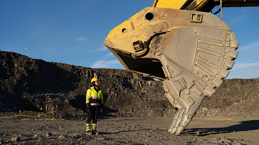 A person standing next to a giant truck with a bucket shovel on it.