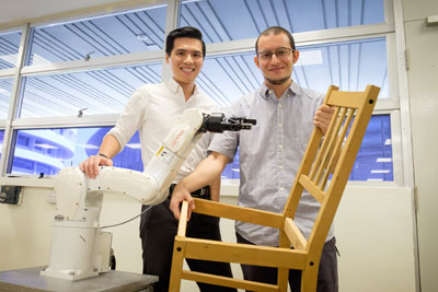 Researchers posing with a robotic arm and a chair assembled by the robot.