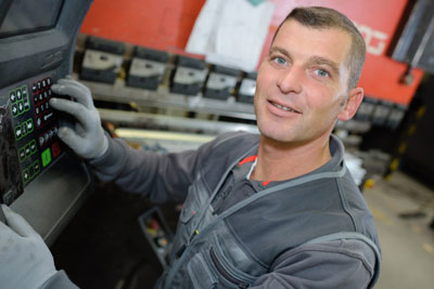 A photograph of a specialized factory worker at an interface panel for automation machinery.