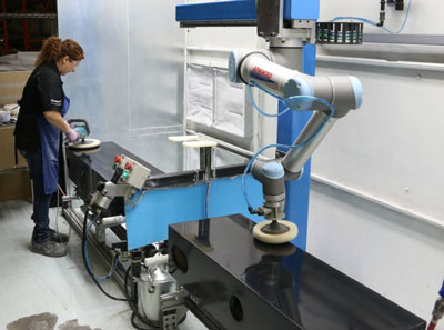 A photo of a woman working alongside a robot to polish speaker cabinets.