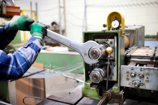 An image of a factory maintenance worker adjusting a machine with a large wrench.