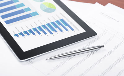 A photo of charts and graphs on a tablet with printed data sheets on a table