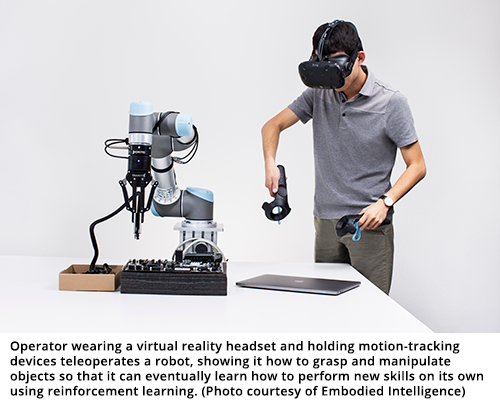 Operator wearing a virtual reality headset and holding motion-tracking devices teleoperates a robot, showing it how to grasp and manipulate objects so that it can eventually learn how to perform new skills on its own using reinforcement learning. (Photo courtesy of Embodied Intelligence)